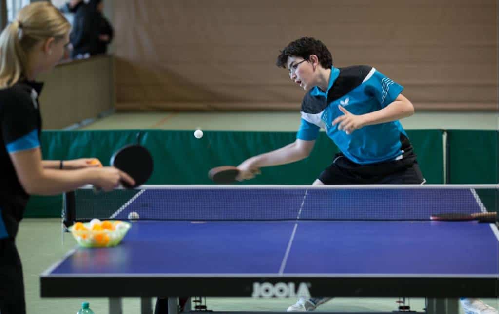 Schnelles Tischtennisspiel zwischen zwei Spielern bei CK-Tischtennis, Fokus auf profimäßiges Training, Anfänger und Turniere, mit hochwertigen Schlägern und Bällen in einer Hallenumgebung.