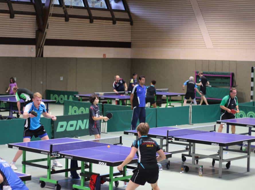 Modernes Tischtennistraining in einer Indoor-Halle mit mehreren Tischen und Spielern unterschiedlichen Alters, ideal für Tischtennis-Training und -Wettkämpfe im Verein.