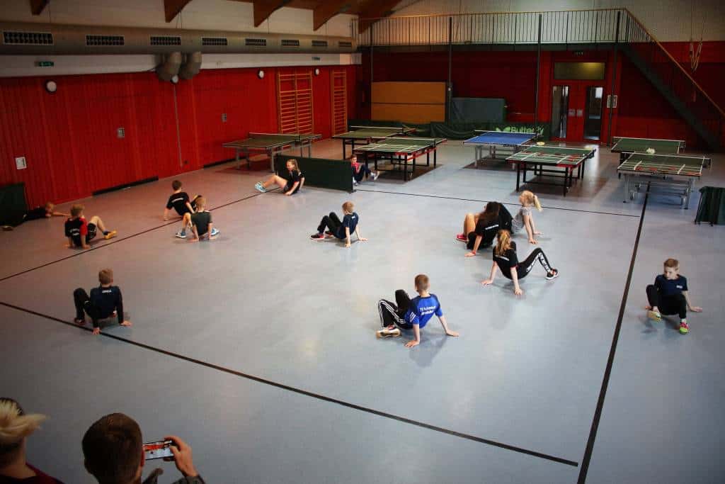 Schüler beim Tischtennistraining in der Turnhalle, mit mehreren Tischen und jungen Spielern, die Übungen machen, förderndes Training im Tischtennisverein CK-Tischtennis in Deutschland.