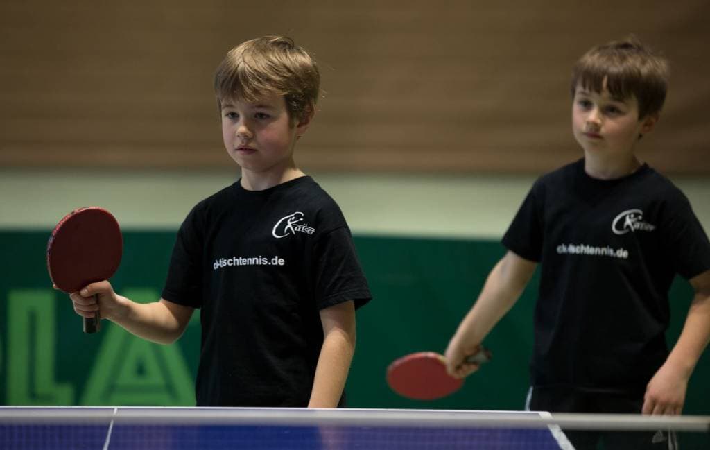 Kinder beim Tischtennistraining, focused auf das Spiel, beide halten Paddel, in Trainingskleidung mit CK-Tischtennis Logo.